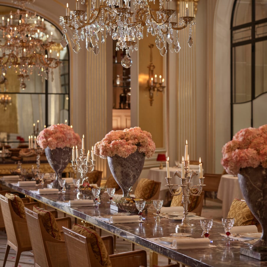 Jean Imbert au Plaza Athénée的中央大理石桌子，粉红色的花朵和枝形吊灯。水晶吊灯悬挂在桌子上方。酒店广场Athénée，巴黎
