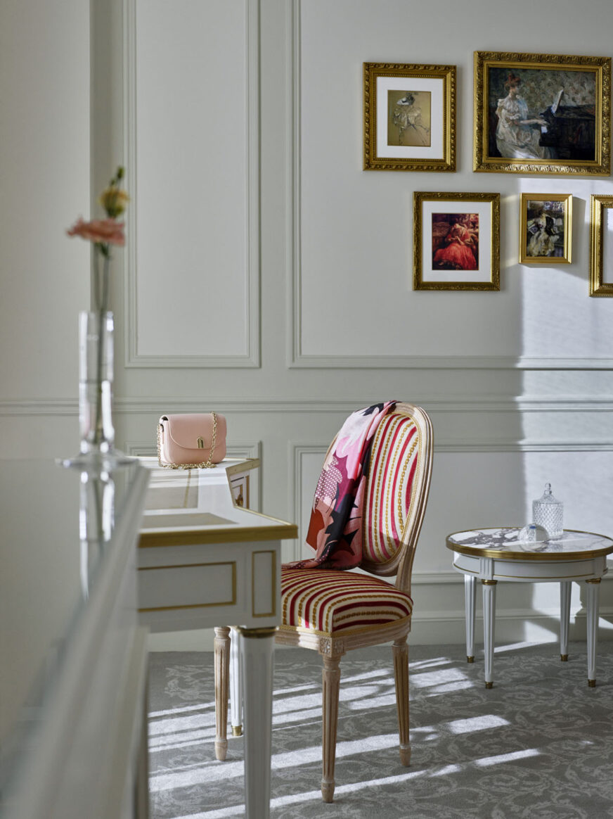 照片d'une sacoche玫瑰posée sur une table blanche et dorée accompagnée de une chise rayée de couleur玫瑰紫红色et dorée, situées dans la Suite Deluxe au sein de l'hôtel Le Meurice à巴黎。