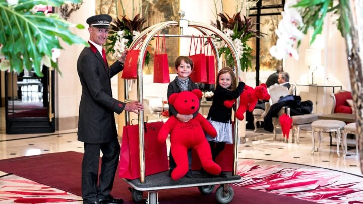 两个孩子在广场大厅的行李车上玩红色泰迪熊古斯塔夫Athénée