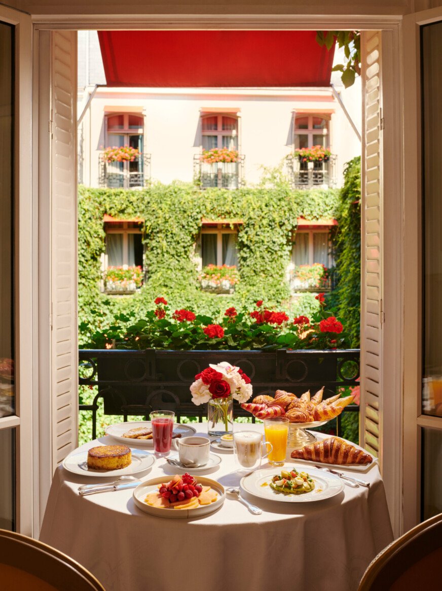 在巴黎Hôtel广场Athénée，早餐桌摆放在面向La Cour Jardin常春藤的窗户前。