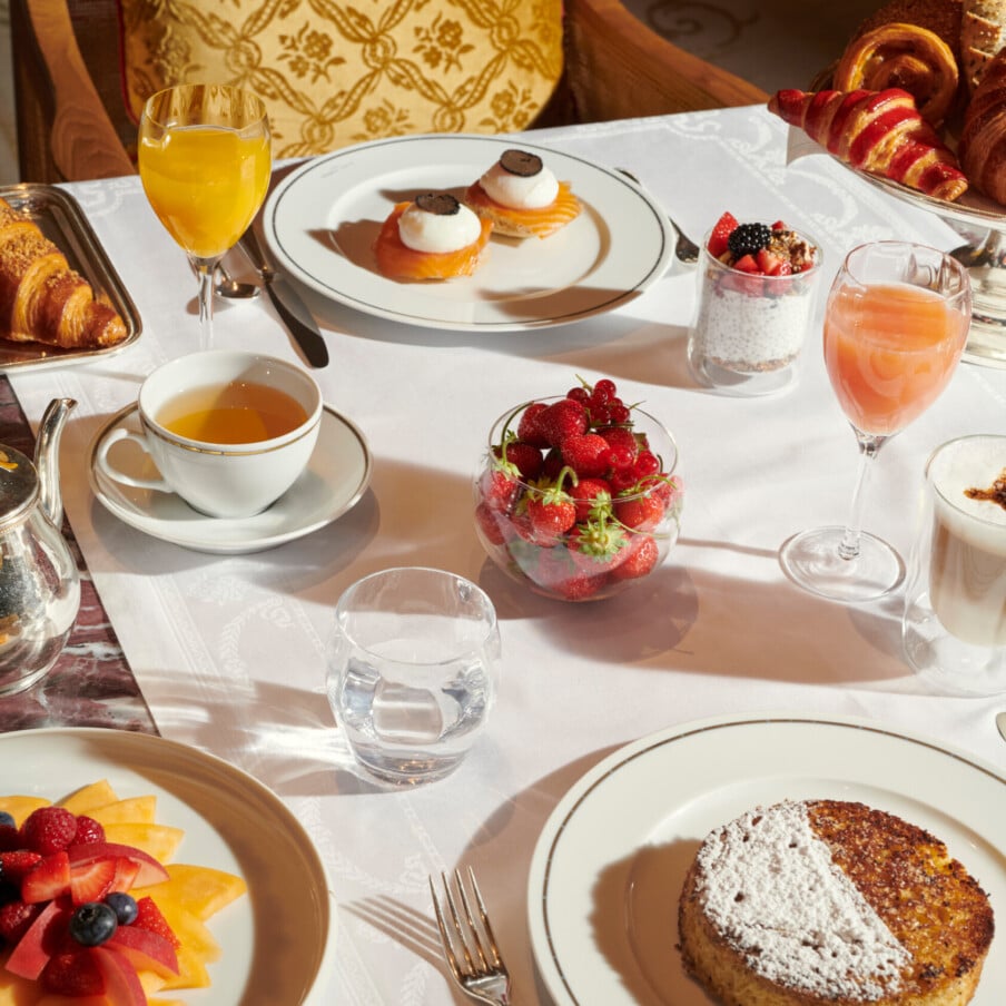 我们的主餐厅Hôtel Plaza Athénée的早餐桌，放在白色桌布上，有煎饼、松露鸡蛋、水果盘和草莓，旁边有饮料。
