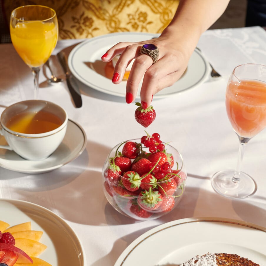 早餐桌上有一碗草莓，还有一只手在摘草莓。